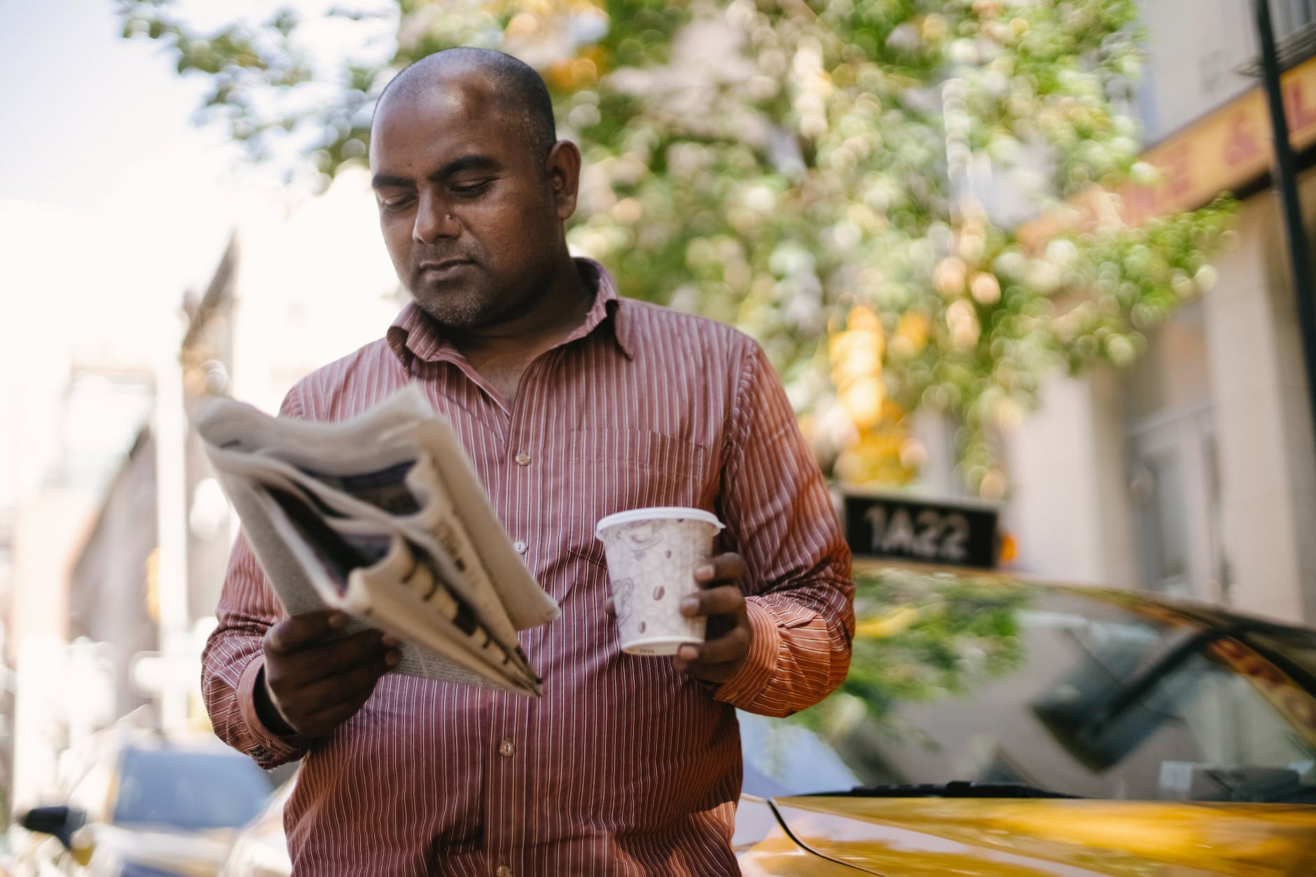 serious ethnic cab driver with takeaway coffee and newspaper